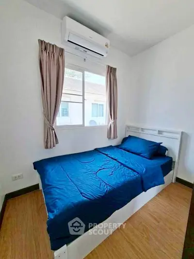 Cozy bedroom with blue bedding, air conditioning, and natural light from window.