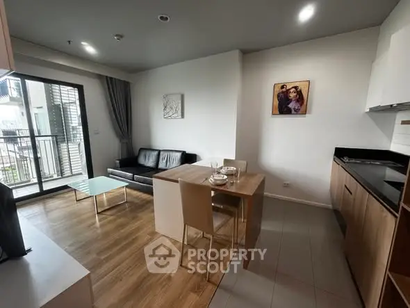 Modern open-plan living room with kitchen and balcony access, featuring sleek furniture and wooden flooring.