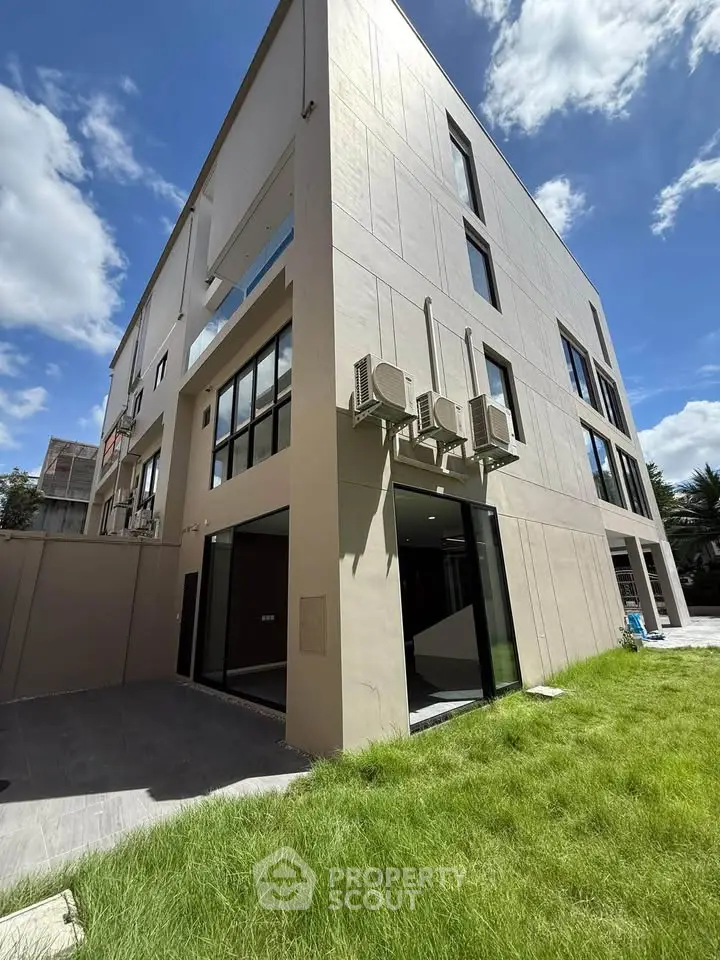 Modern three-story building with large windows and lush green lawn under a bright blue sky.