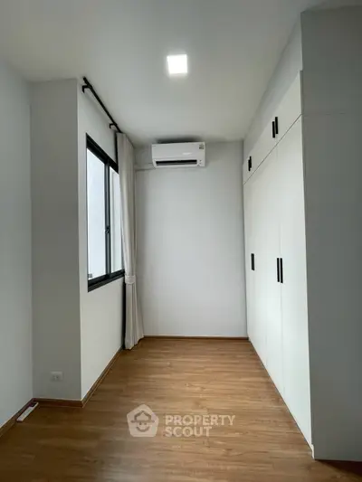 Spacious bedroom with wooden flooring and built-in wardrobe, featuring air conditioning and natural light.