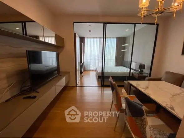 Modern apartment interior with open living and dining area leading to a bedroom through glass doors.