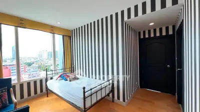Stylish bedroom with striped walls and city view, featuring a cozy bed and wooden flooring.