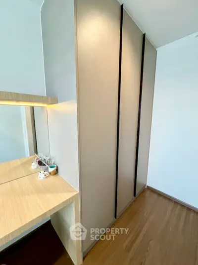 Modern bedroom with sleek wardrobe and wooden flooring, featuring a stylish vanity area with mirror.