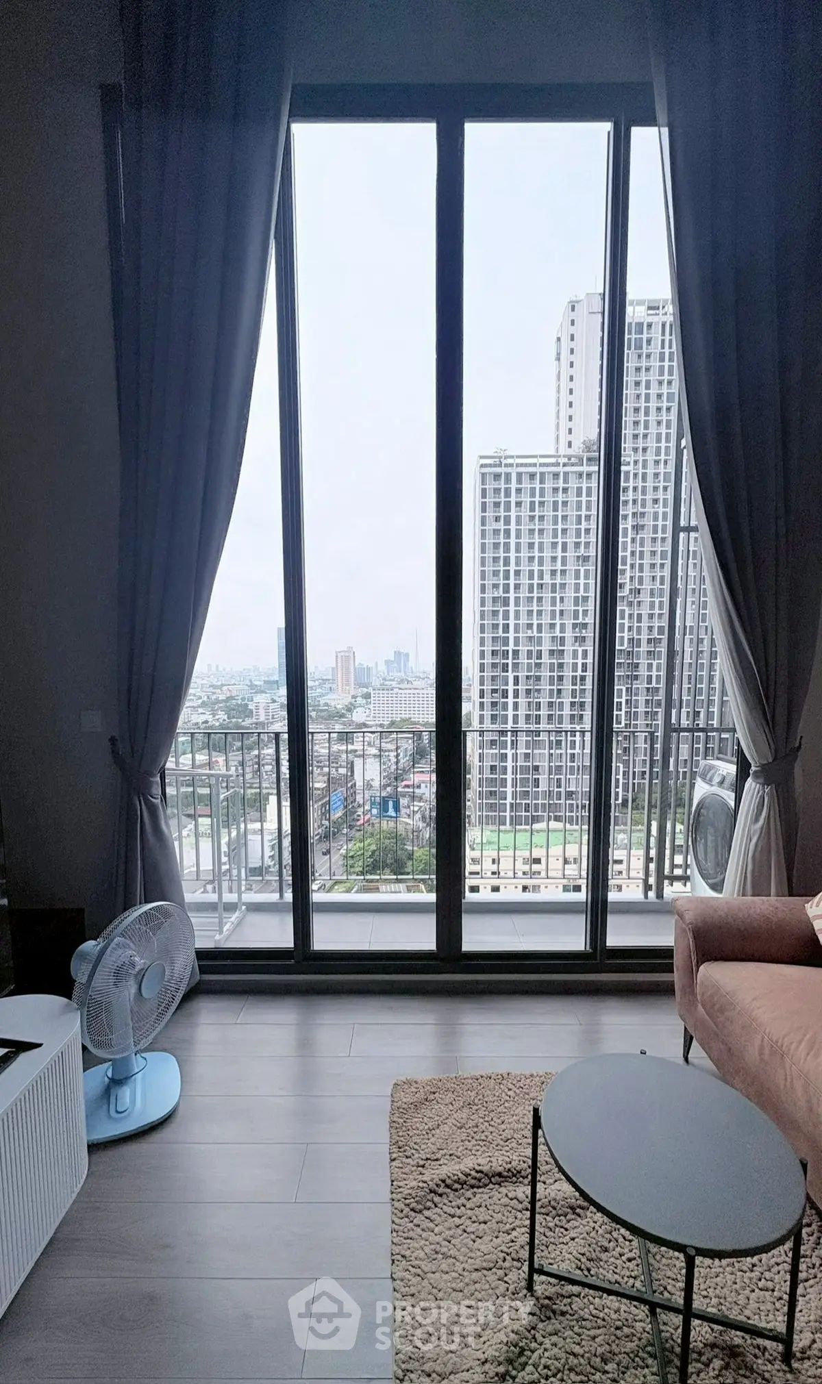 Modern living room with large windows offering stunning city views and cozy furnishings.