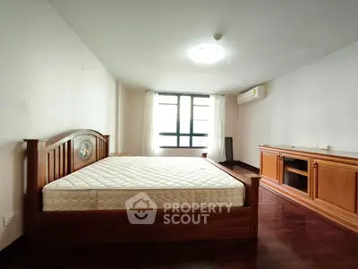 Spacious bedroom with wooden furniture and large window for natural light.