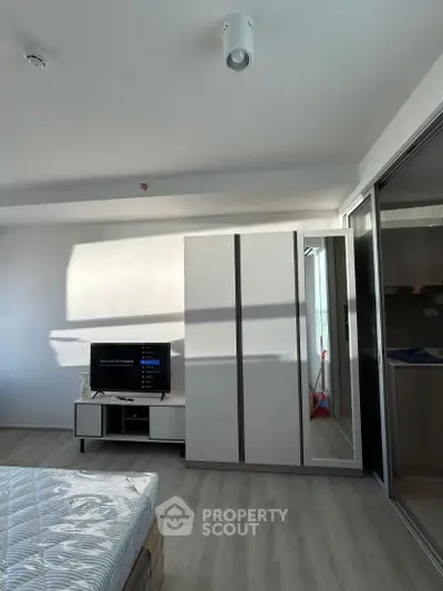 Modern bedroom with sleek wardrobe and TV unit, featuring natural light and minimalist design.