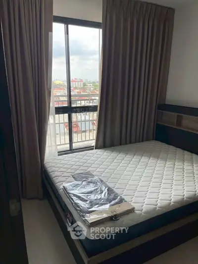 Cozy bedroom with large window offering city views, featuring a comfortable mattress and elegant curtains.