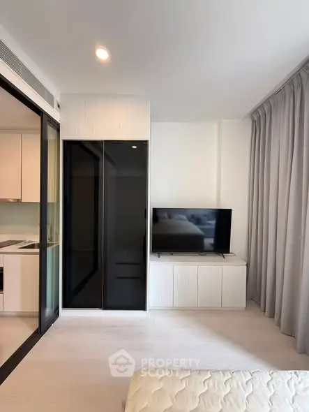 Modern living room with sleek design and large TV, adjacent to a stylish kitchen.