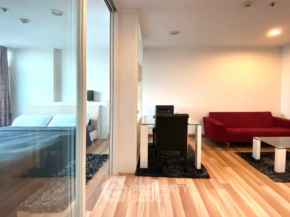 Modern apartment interior with glass partition, featuring a cozy bedroom and stylish living area with red sofa.