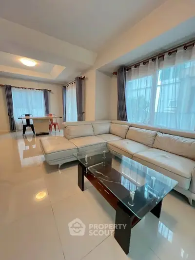 Spacious living room with elegant sectional sofa and glass coffee table, featuring large windows and modern decor.
