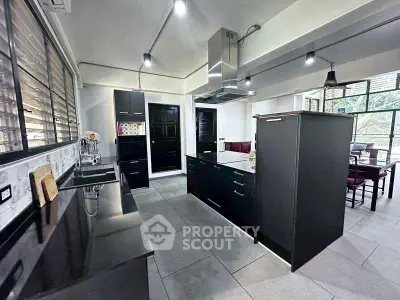 Modern kitchen with sleek black cabinetry and open layout, featuring stainless steel appliances and ample natural light.