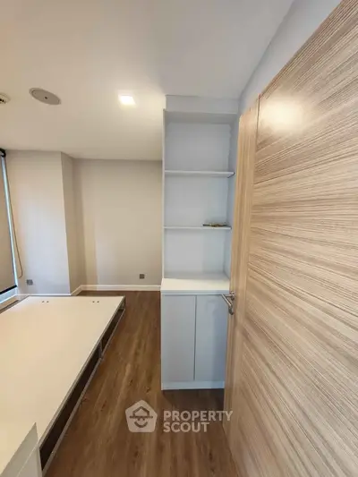 Modern bedroom with wooden flooring and built-in shelves, showcasing minimalist design.