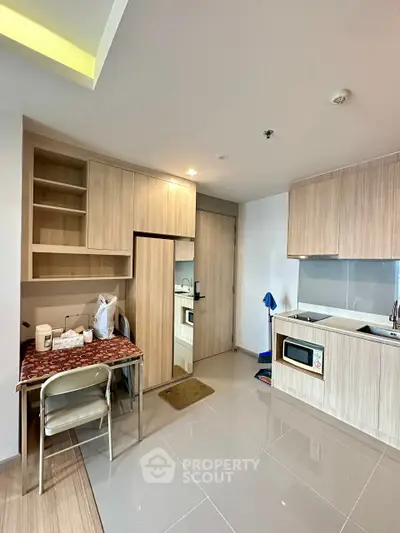 Modern studio apartment with compact kitchen and dining area, featuring sleek cabinetry and tiled flooring.