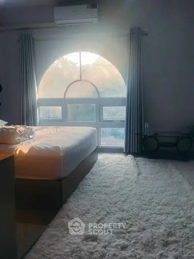 Cozy bedroom with large arched window and plush carpet, perfect for relaxation.