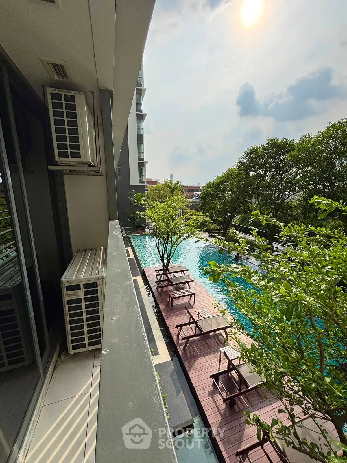Stunning poolside view from balcony with lush greenery and sunlit ambiance.