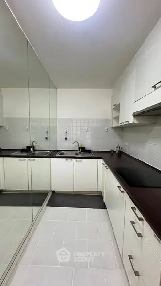 Modern kitchen with sleek white cabinets and mirrored wall for spacious feel.