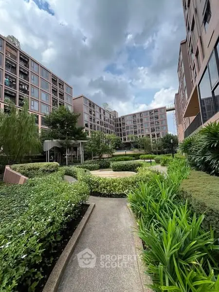 Modern residential complex with lush green garden and pathway under cloudy sky.