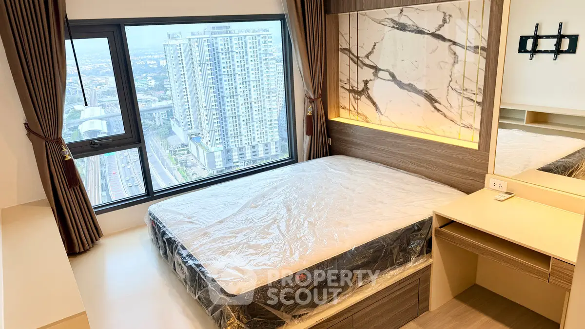 Modern bedroom with large window offering stunning city views in a high-rise apartment.