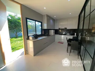 Spacious modern kitchen with sleek cabinetry and high-end appliances, opening onto a sunlit garden through large glass doors, perfect for entertaining.