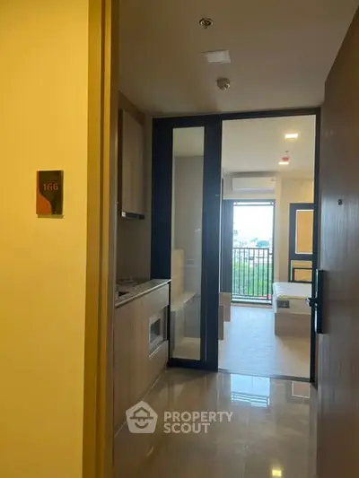 Modern apartment entrance with sleek kitchen and bright living area leading to balcony.
