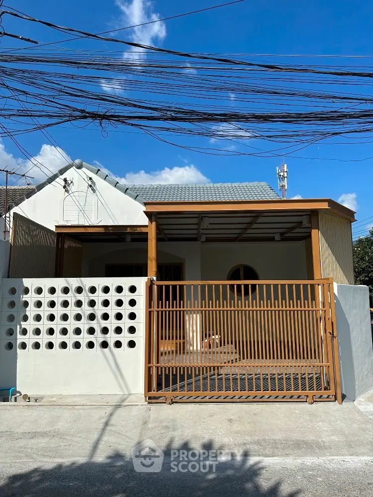 Charming single-story house with modern facade and gated entrance in sunny neighborhood.