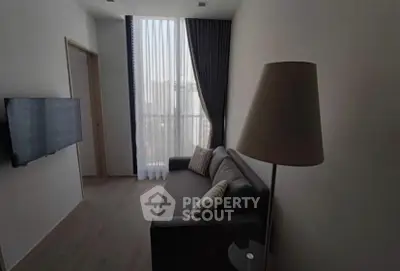 Modern living room with sleek sofa and floor lamp, featuring tall windows and elegant curtains.