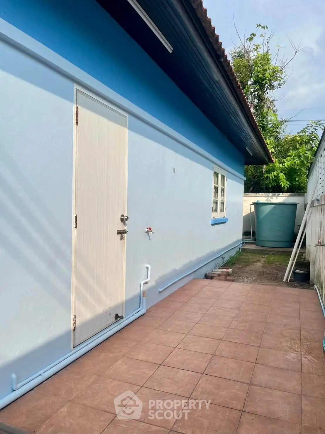 Charming blue exterior with tiled patio and lush greenery, perfect for serene outdoor living.