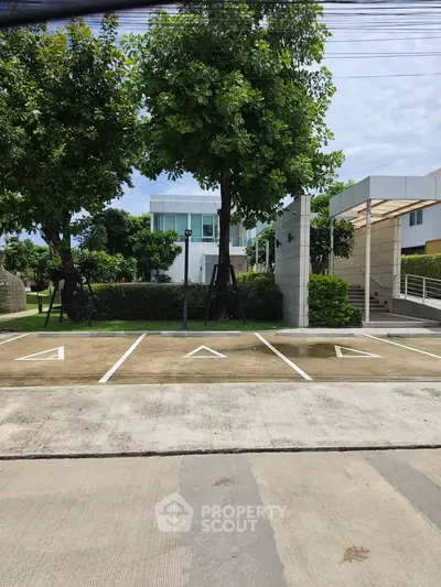 Modern building exterior with lush greenery and spacious parking area.