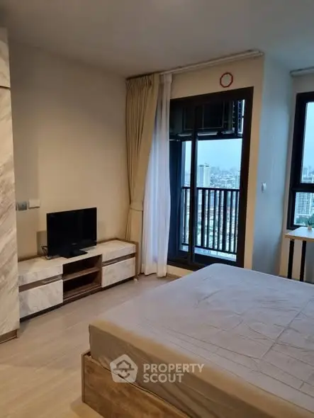 Modern bedroom with city view and balcony access in high-rise apartment.