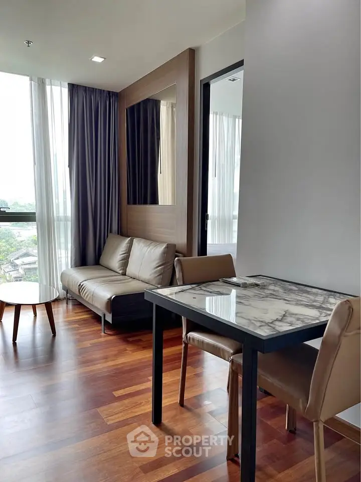 Modern living room with elegant marble dining table and cozy seating area, featuring large windows and wooden flooring.