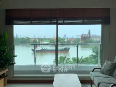 Stunning river view from a modern living room with large windows and lush greenery.