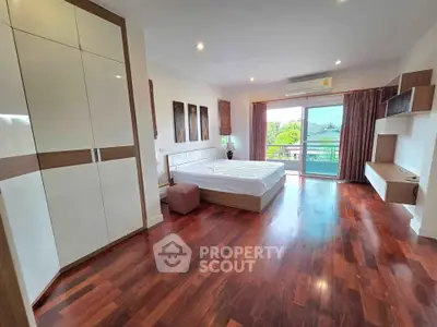 Spacious bedroom with wooden flooring and balcony view in modern apartment