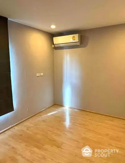 Spacious empty room with wooden flooring and air conditioning unit