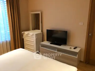 Cozy bedroom with TV and dresser, warm lighting, perfect for relaxation.