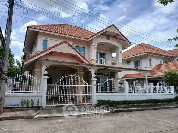 Charming two-story house with red-tiled roof and white fence in a suburban neighborhood.