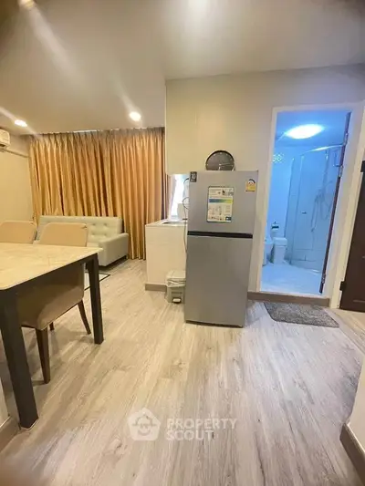Modern apartment interior with open layout, featuring a cozy living area and a compact kitchen with a fridge.