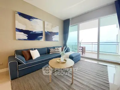 Modern living room with stylish blue sofa, abstract art, and large balcony with ocean view.