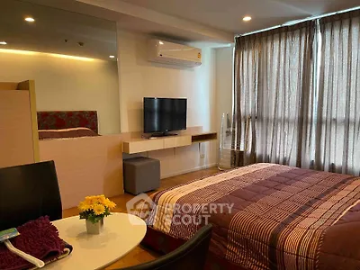 Cozy bedroom with modern decor, featuring a wall-mounted TV and large window with curtains.
