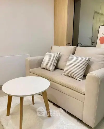 Cozy living room with beige sofa, striped cushions, and round white coffee table on plush rug.