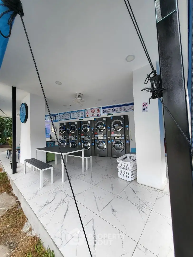 Modern laundry facility with multiple washing machines and seating area in a sleek, tiled space.