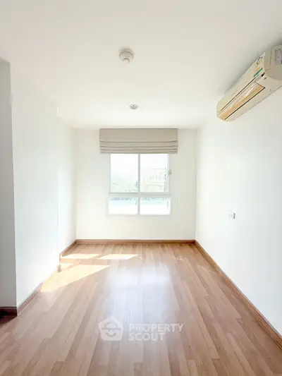 Bright empty room with wooden flooring and air conditioning unit, ideal for customization.