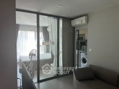 Modern apartment with glass partition, cozy living area, and washing machine in view.