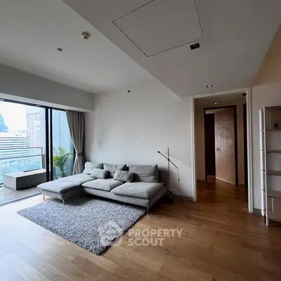 Modern living room with large windows and city view, featuring a cozy gray sofa and wooden flooring.