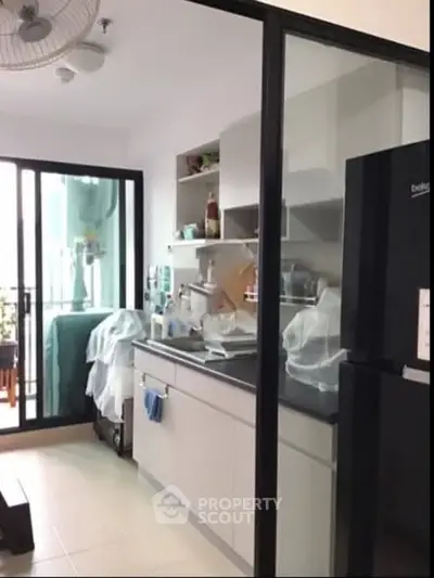 Modern kitchen with sleek cabinetry and balcony access, featuring a black refrigerator and ample storage.