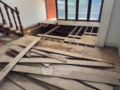 Spacious living room under renovation with large windows and wooden staircase.