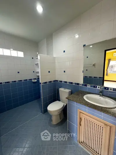Spacious bathroom with modern blue and white tile design, featuring a toilet and sink with a large mirror.