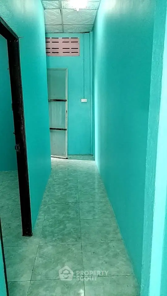 Narrow turquoise hallway with tiled floor and open door at the end