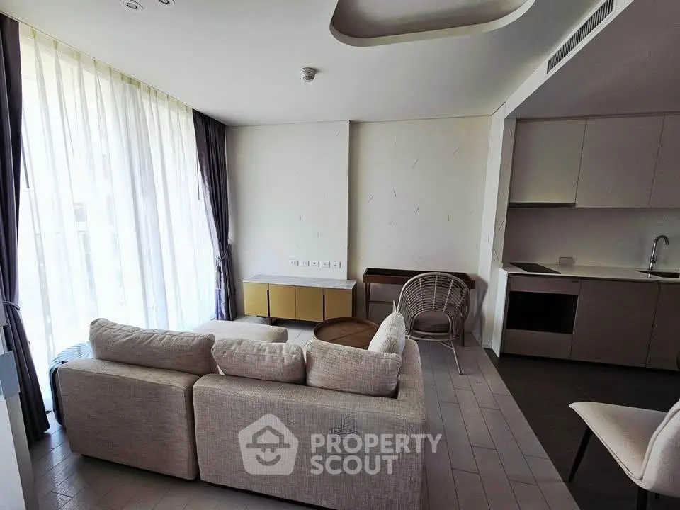 Modern living room with open kitchen, featuring sleek furniture and large windows for natural light.