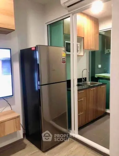 Modern kitchen with sleek fridge and stylish cabinetry in compact apartment.