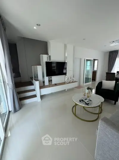 Modern living room with sleek design, featuring a flat-screen TV, stylish furniture, and large windows for natural light.
